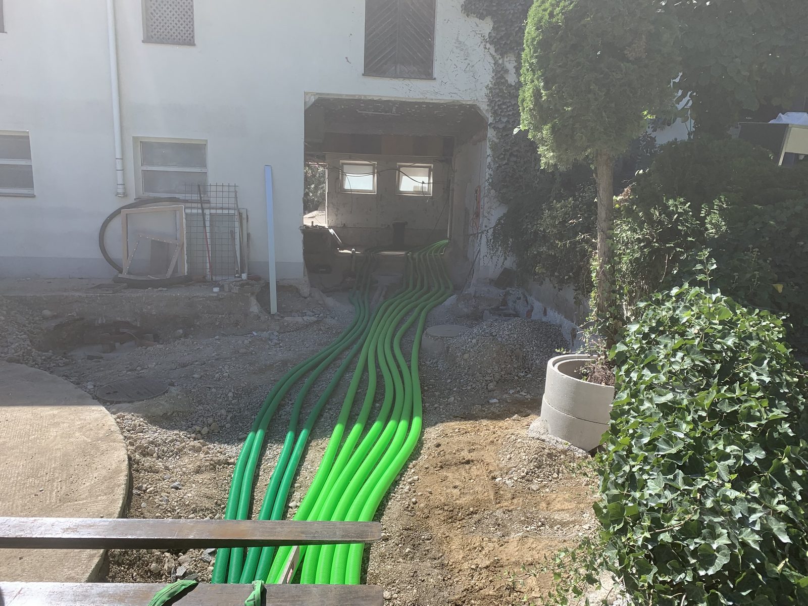 Baustelle am Hof: zehn grüne Wellrohre liegen im offenen Graben und laufen durch die Kellermauer ins Gebäude.